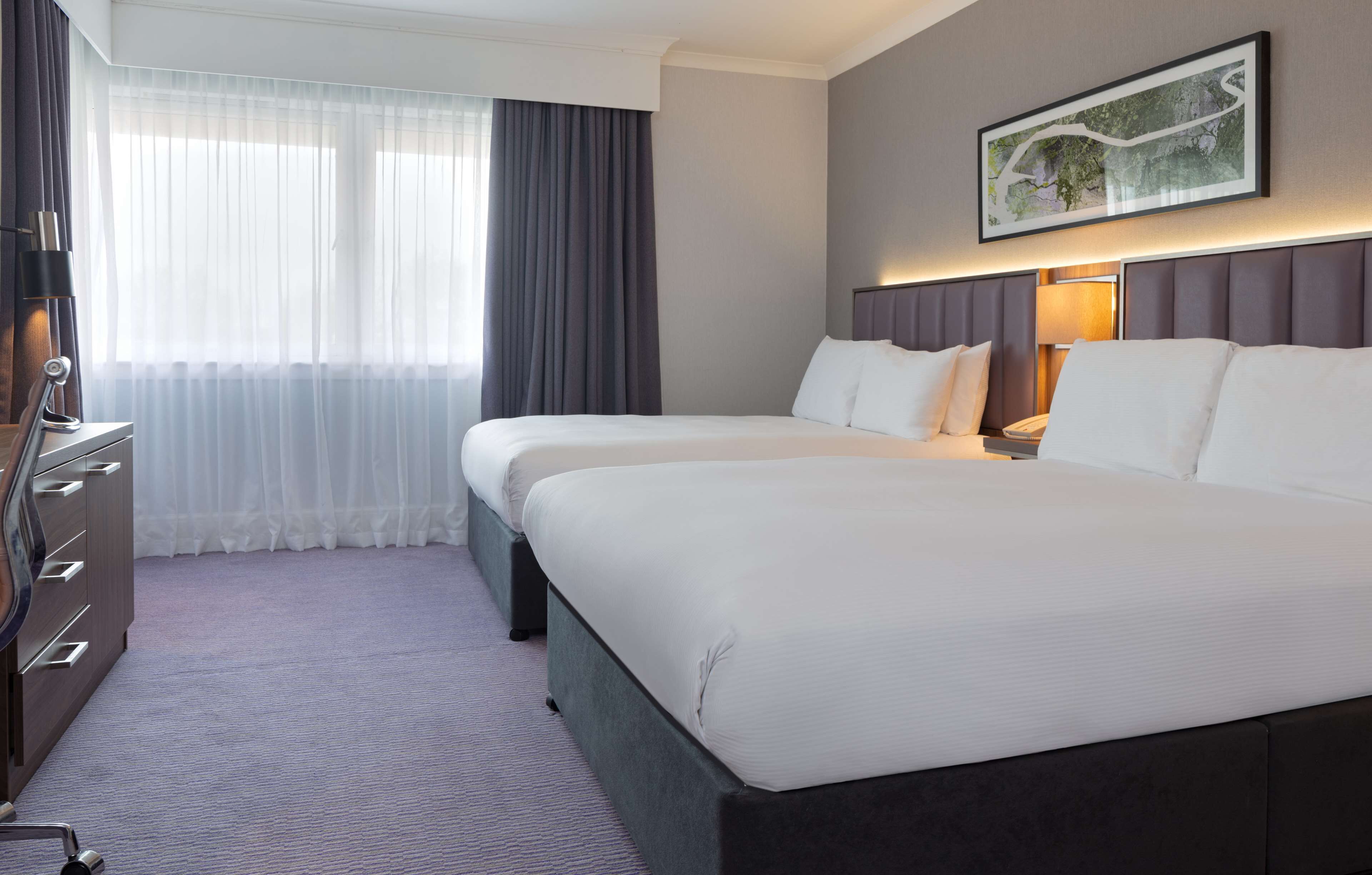 A hotel room with two beds, a desk, a chair, and a large window with curtains.