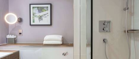 Une salle de bain moderne avec une douche à l’italienne en verre, une œuvre d’art encadrée au mur et un miroir rond avec un éclairage intégré.
