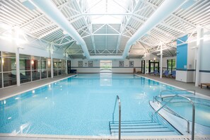 An indoor swimming pool with clear blue water, surrounded by lounge chairs and a high ceiling with a geometric design. - DoubleTree by Hilton Edinburgh Airport (Newbridge)