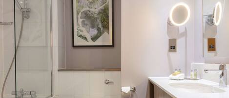 A modern bathroom with a glass-enclosed shower, a toilet, a sink with a mirror, and a framed abstract painting on the wall.