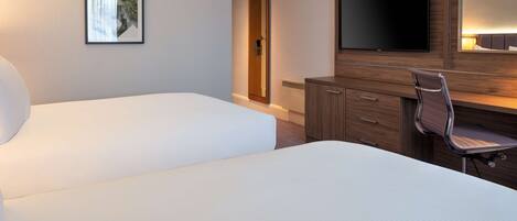 A hotel room with two beds, a TV, a desk with a chair, and a framed picture on the wall.