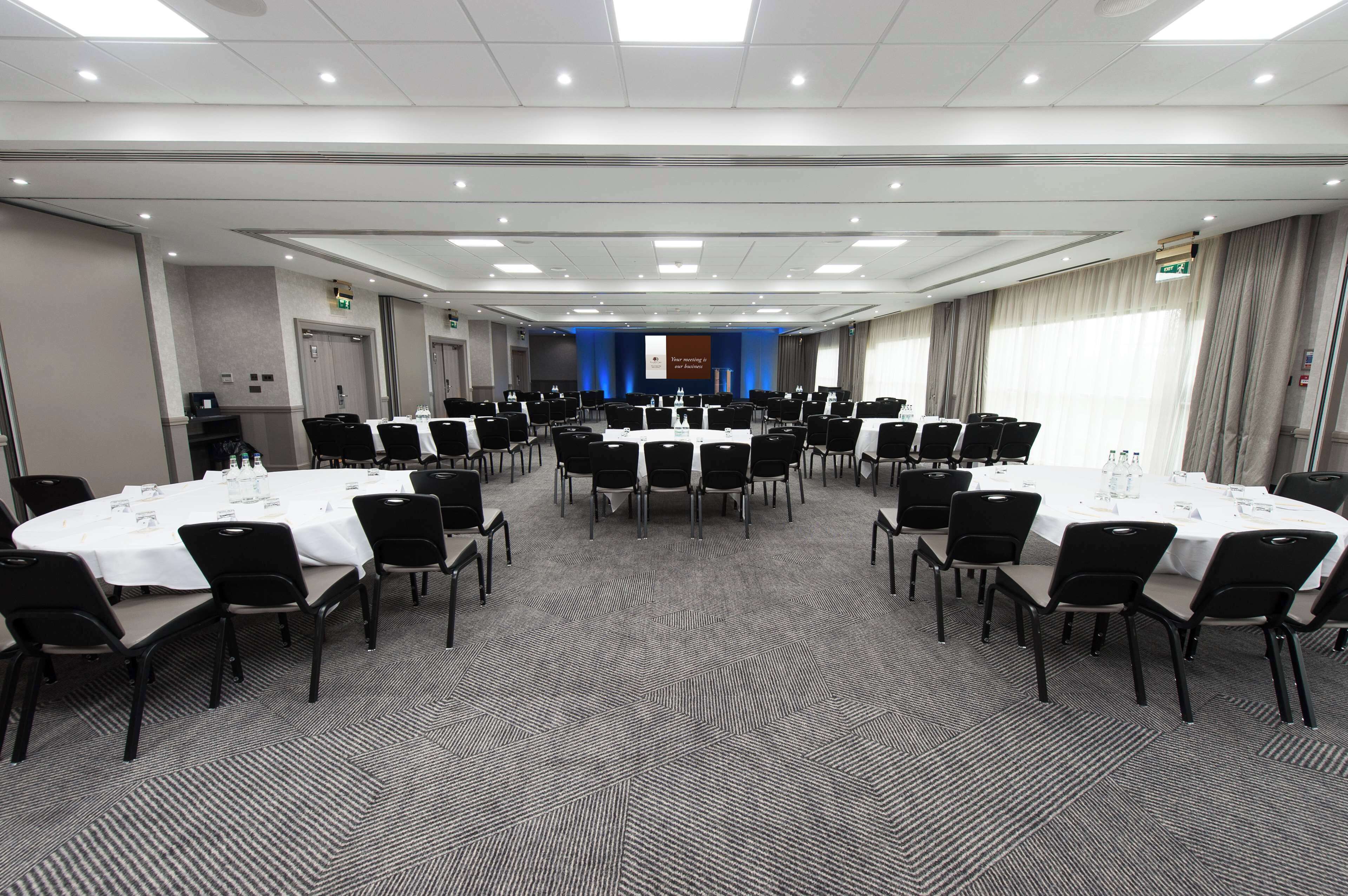 A conference room with multiple round tables and chairs, equipped with water bottles and nameplates.
