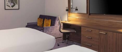 A hotel room with two beds, a desk with a chair, a large mirror, and a framed picture on the wall.
