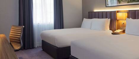 A hotel room with two beds, a desk, a chair, a lamp, and a painting on the wall.