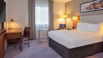 A hotel room with a large bed, a desk, a chair, a small table, and two lamps.