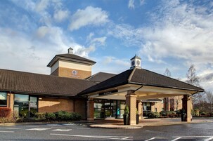 Un hotel DoubleTree con entrada cubierta, fachada de ladrillo y una torre con reloj.