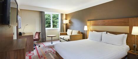 A hotel room with a large bed, a desk, a chair, a TV, and a window with curtains.