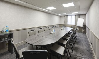 Un salón de conferencias con una larga mesa, sillas, una pantalla de proyector y un dispensador de agua.