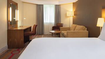 Una camera d'albergo con un letto grande, una scrivania con una sedia, un tavolino rotondo e due poltrone.