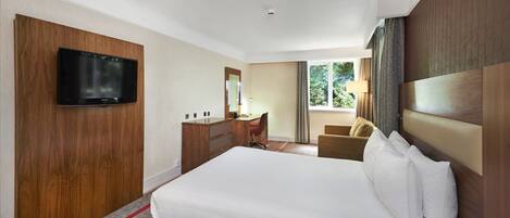 Een hotelkamer met een groot bed, een bureau met stoel, een televisie en een raam met gordijnen.