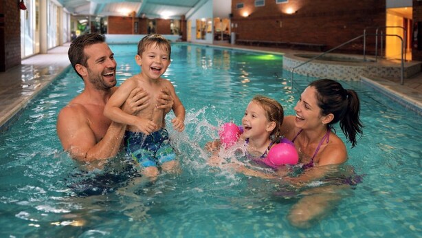 An indoor swimming pool with clear water, a wooden wall, and a staircase leading to an upper level. - ORIDA Hotels Newbury (Newbury)