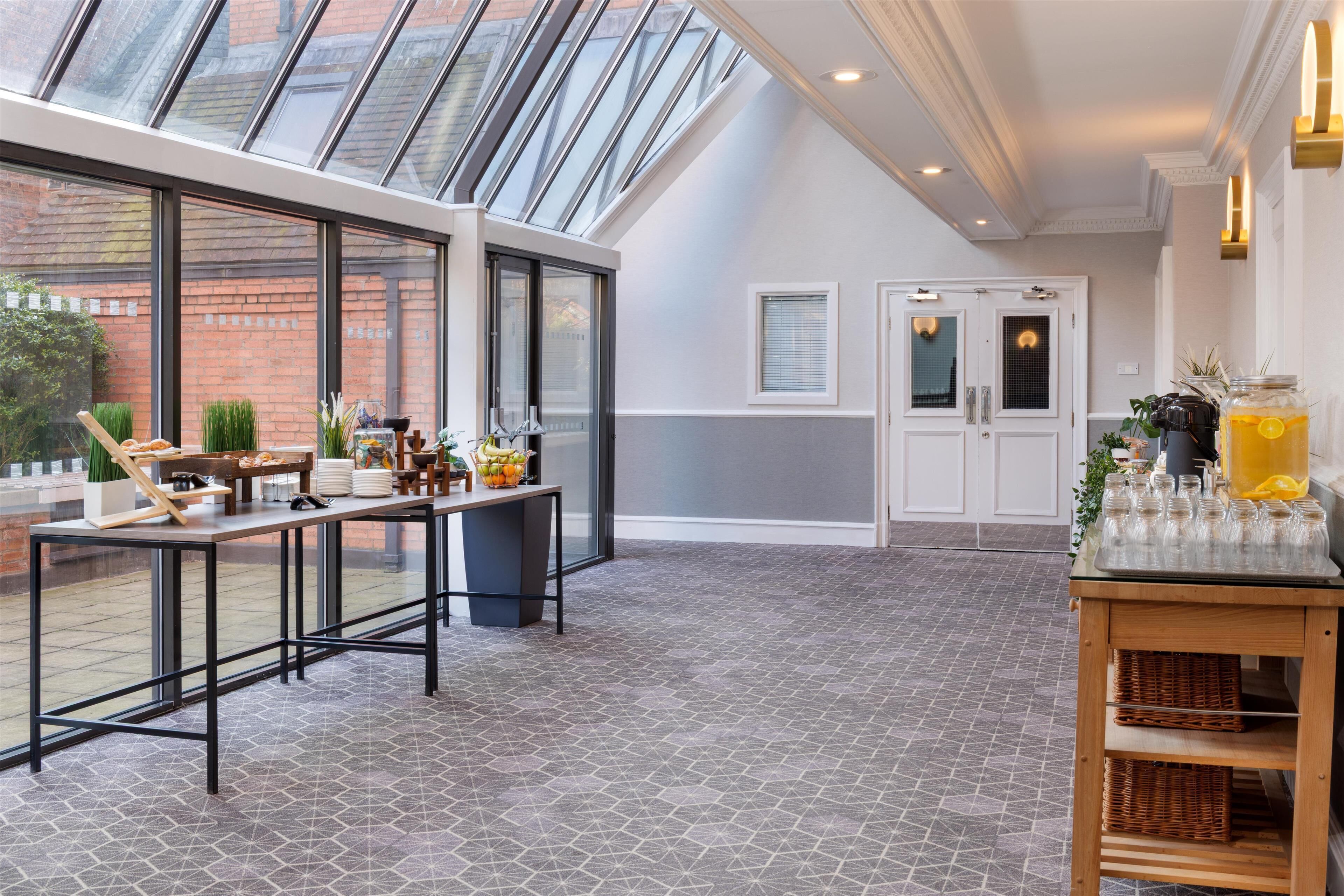 A modern kitchen with a large window, a dining area with a long table, and a small bar area with a drink dispenser.