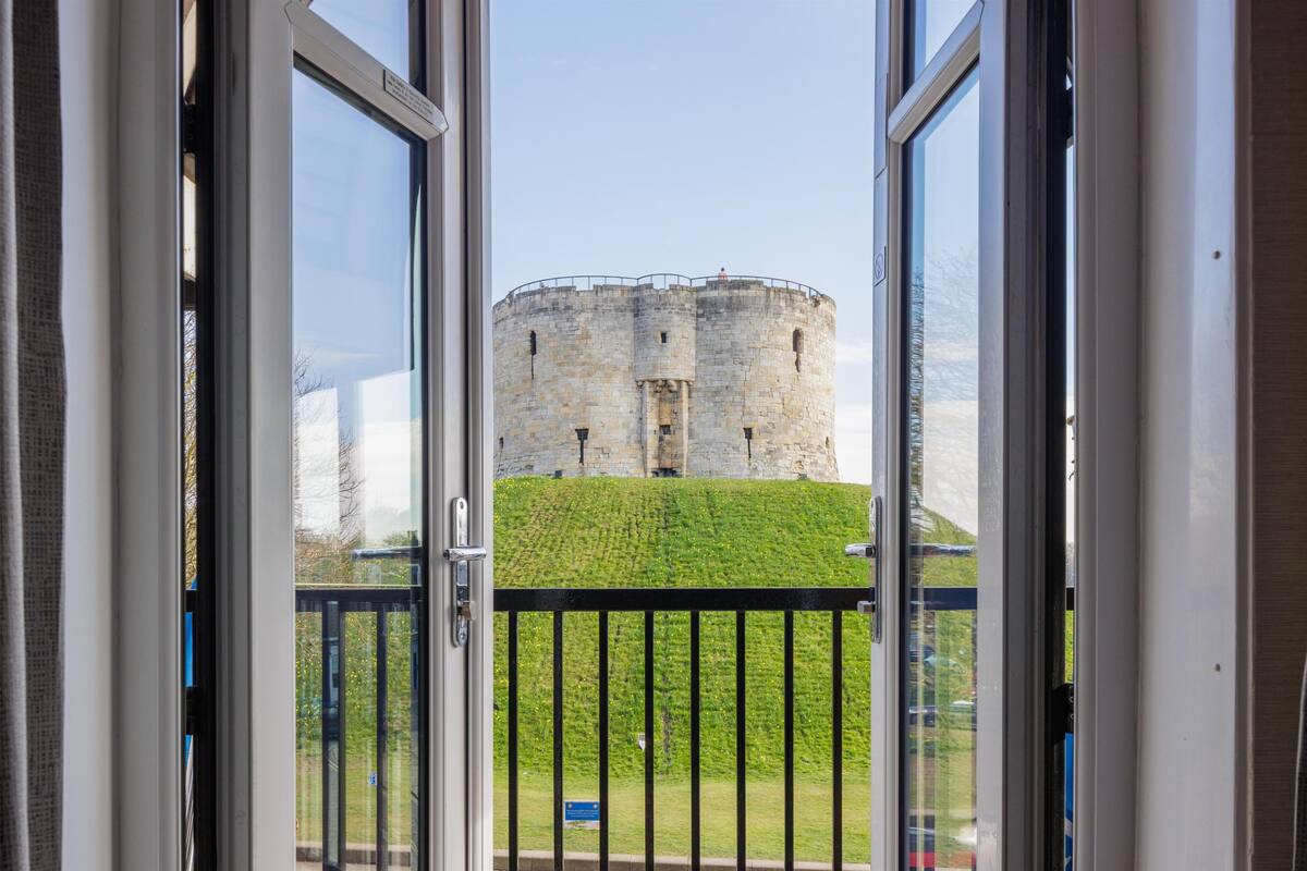 A view of a historic stone tower through a window with a metal railing.