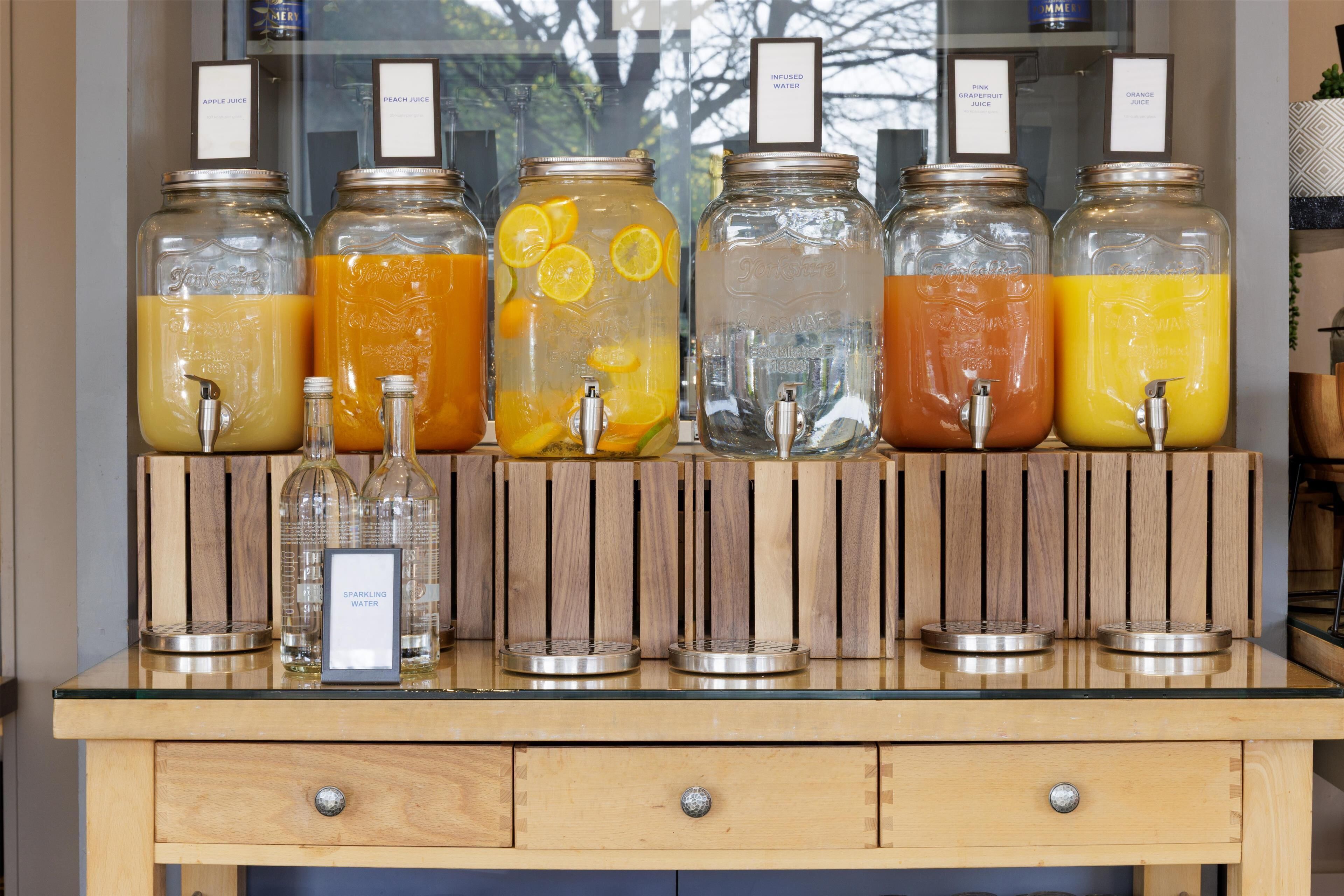 A beverage station with various drink dispensers and a small bottle of sparkling water.
