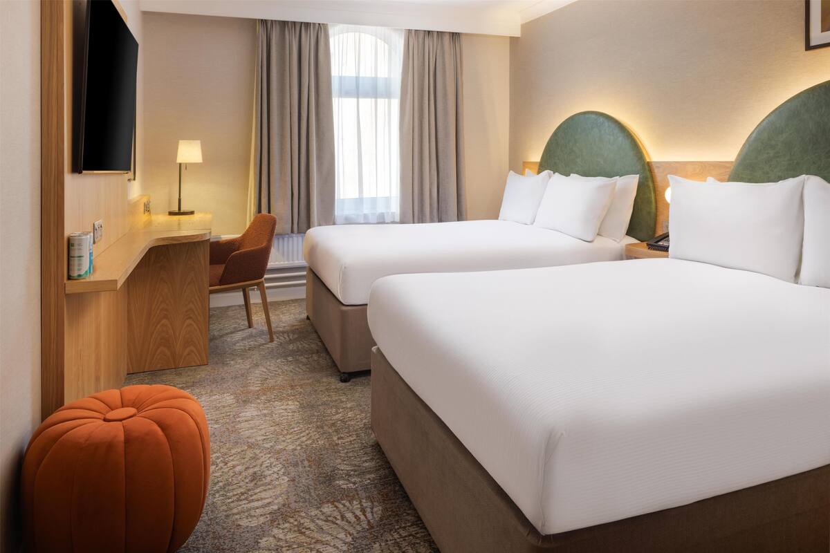 A hotel room with two beds, a desk, a chair, and a TV.