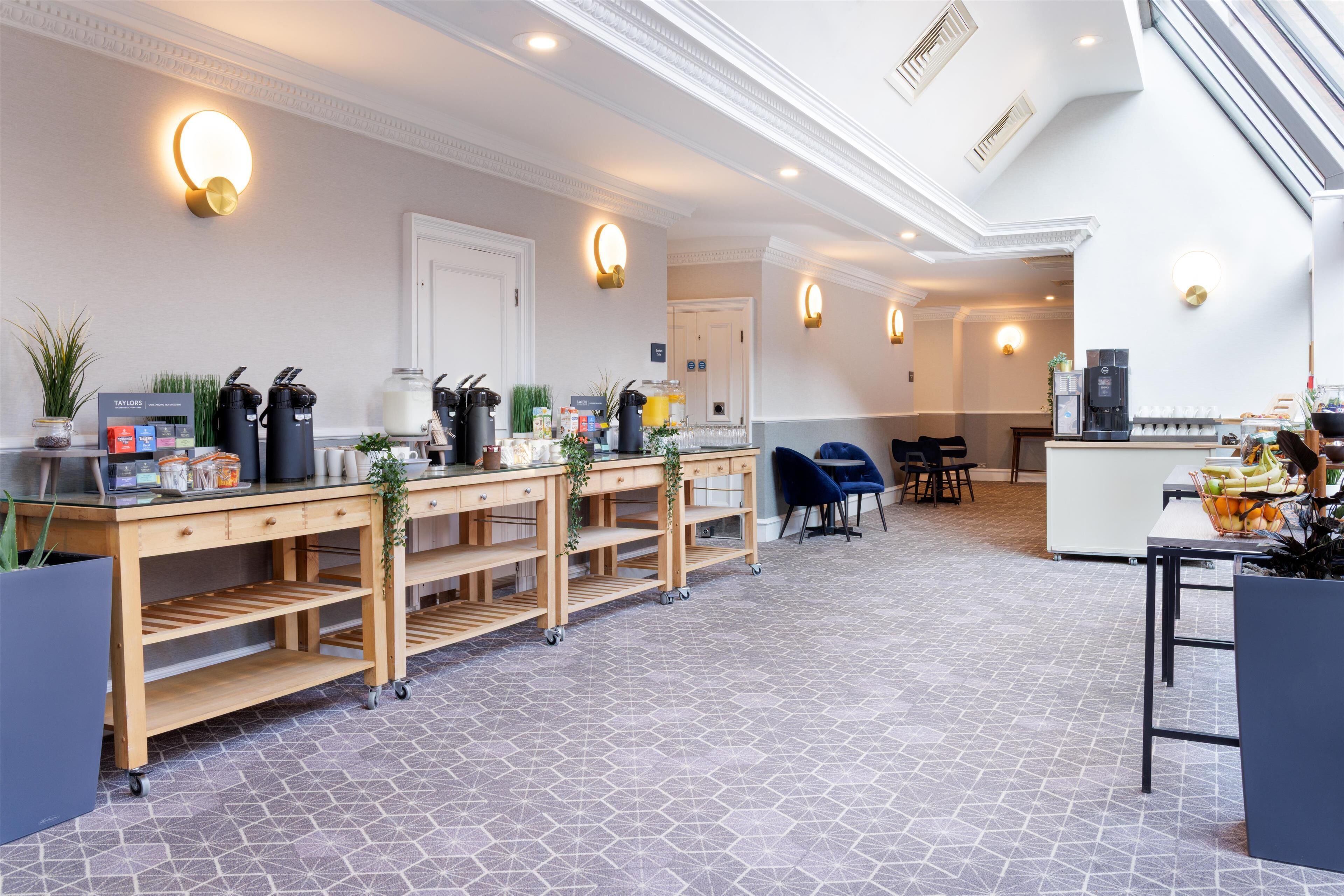 A modern hotel lobby with a reception desk, a coffee station, and a seating area.