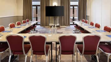 Un salón de conferencias con una larga mesa, sillas rojas, una pantalla grande y vistas al exterior a través de amplios ventanales.