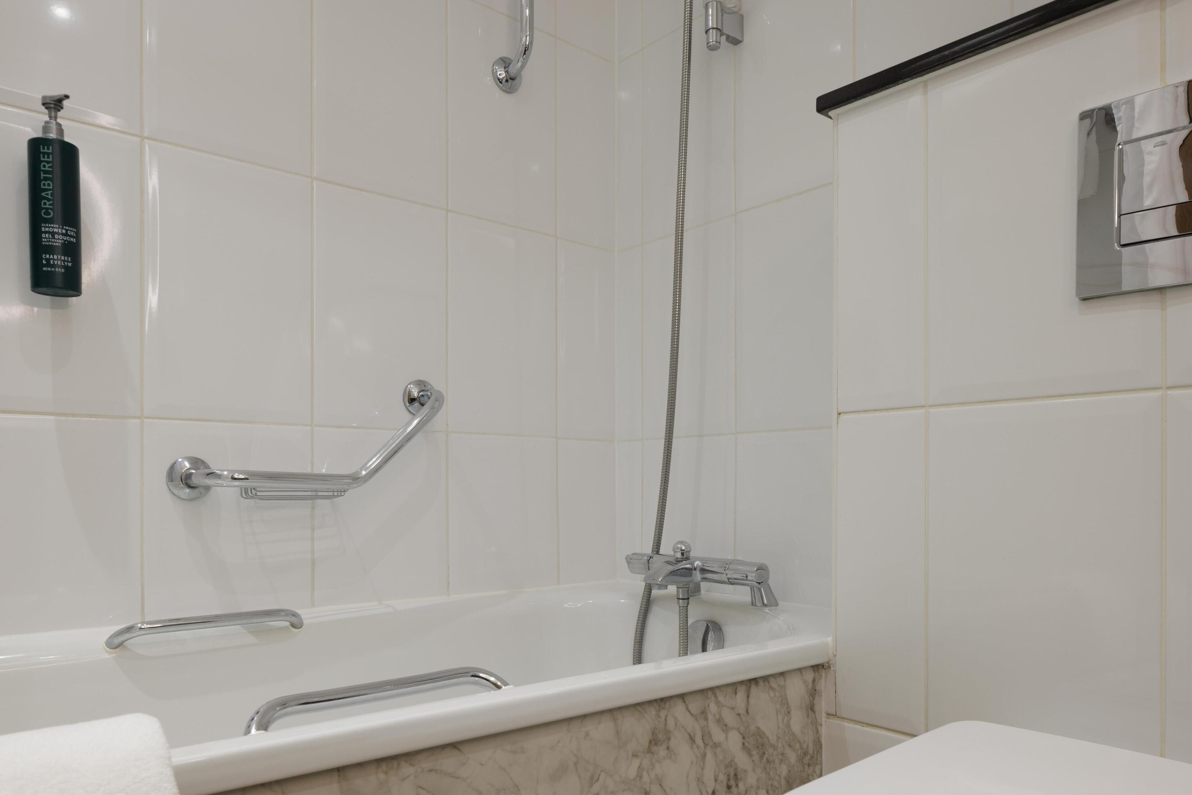 Une salle de bain moderne équipée d’une baignoire, de barres d’appui, d’un pommeau de douche à main et d’un porte-serviettes.