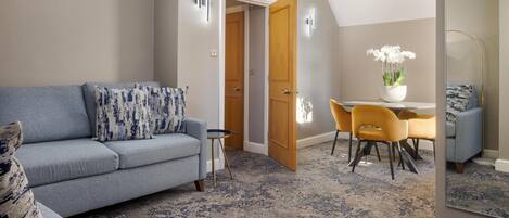A living room with a grey sofa, a dining table with yellow chairs, and a wooden door.