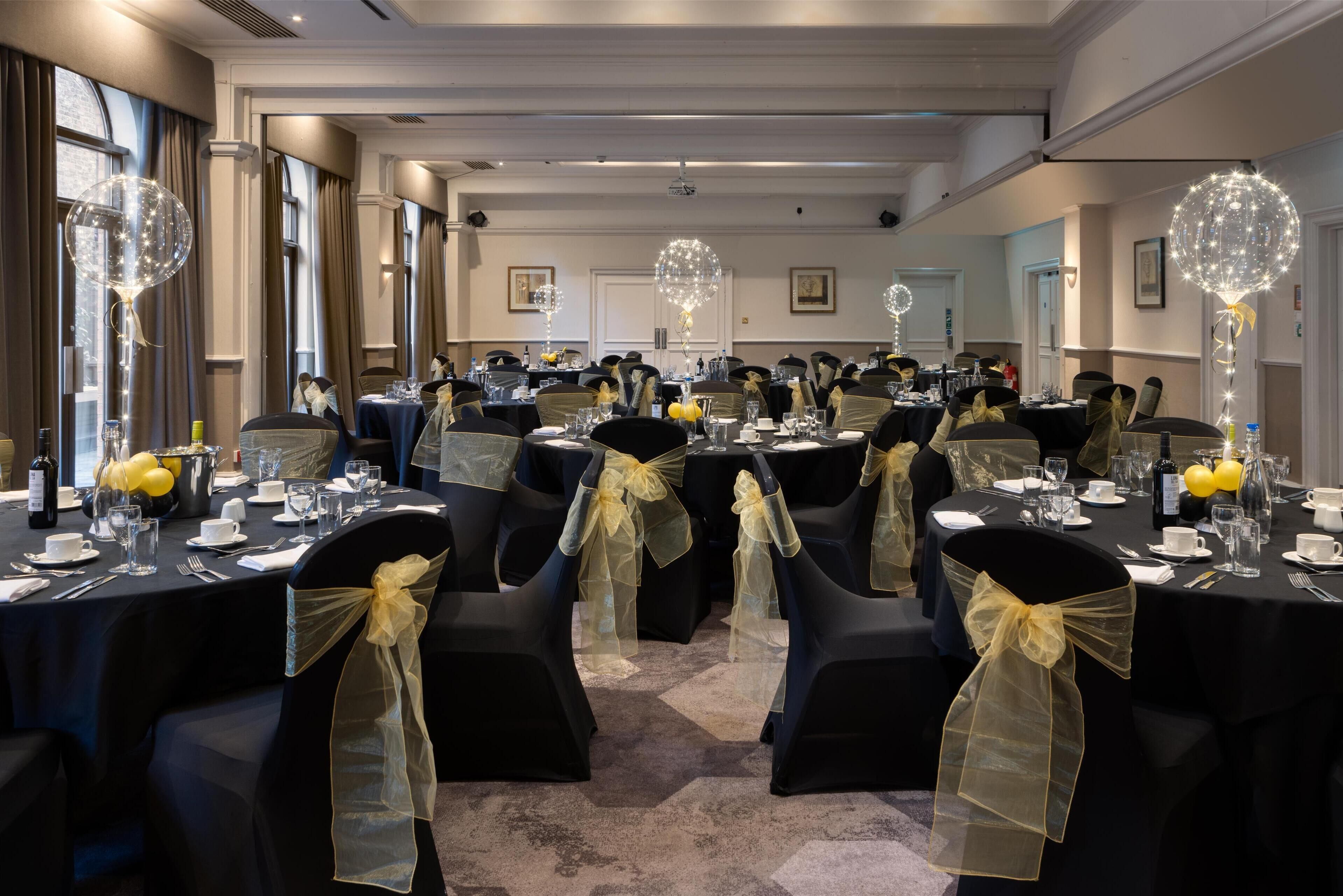 A banquet hall with round tables, chairs with yellow sashes, and decorative light fixtures.