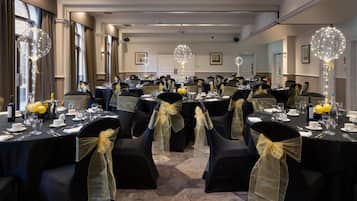 A banquet hall with round tables, chairs with yellow sashes, and decorative light fixtures.