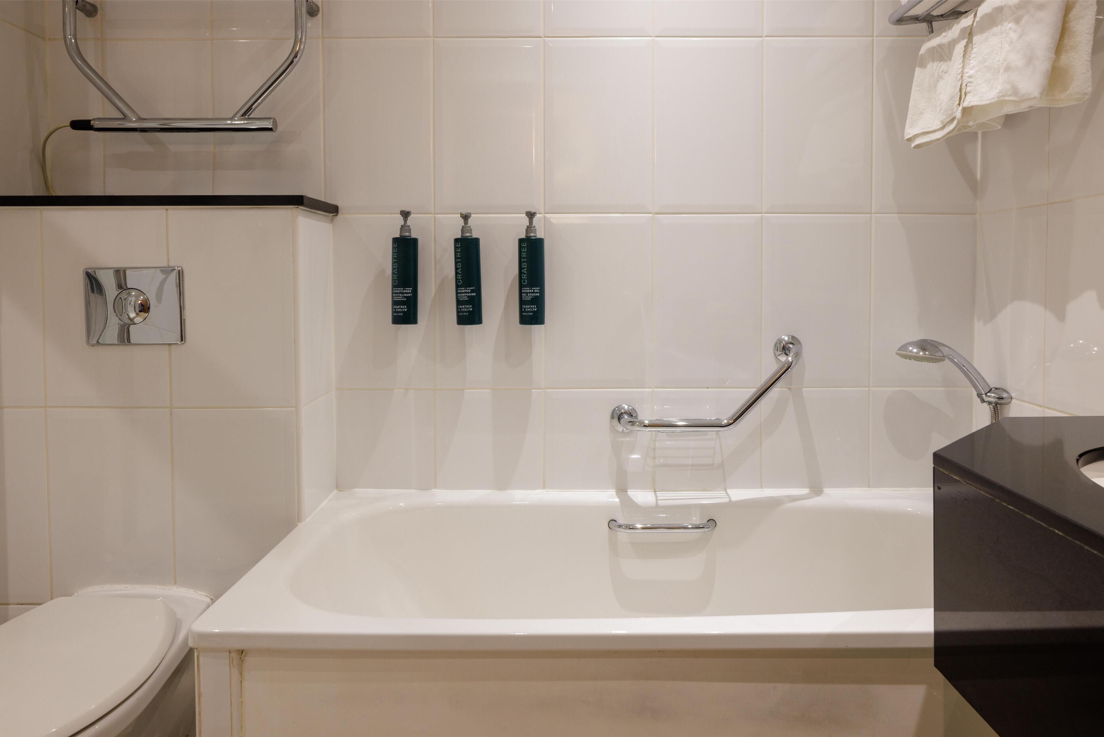A modern bathroom with a bathtub, a toilet, and three toiletries on a shelf.