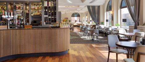 A modern hotel lobby with a bar area, seating arrangements, and large windows.