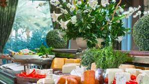 A variety of cheeses and cured meats displayed on wooden boards, with a potted plant and flowers in the background. - Herods Palace Hotel (Eilat)