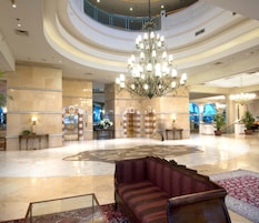 A spacious lobby with a grand chandelier, a central seating area, and a circular floor design.