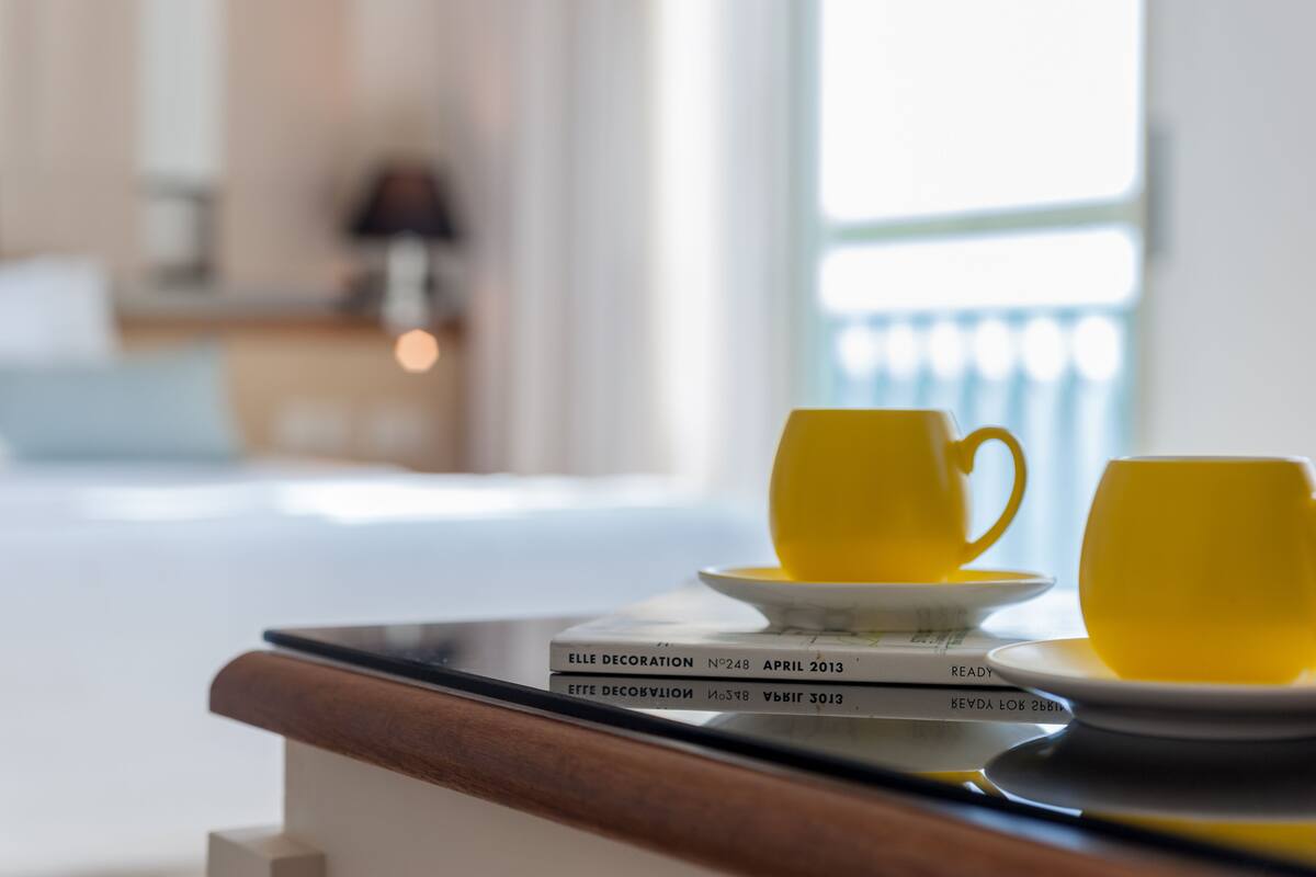 A neatly arranged breakfast table with yellow cups and saucers, a book titled 'ELLE DECORATION', and a lamp in the background.