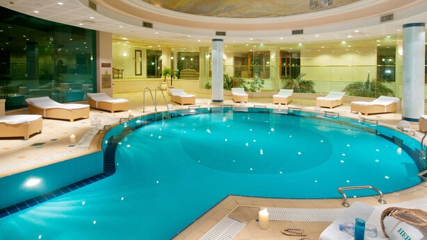 A large indoor swimming pool with lounge chairs and a central column. - Herods Palace Hotel (Eilat)