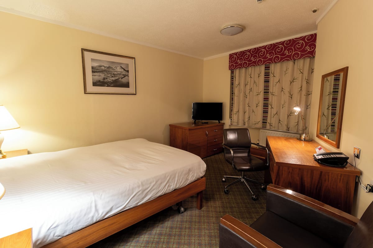 Quarto de hotel com uma cama, uma mesa com cadeira, uma televisão e um espelho.