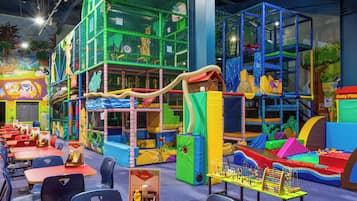 Children can play safely within the enclosed play area featuring climbing nets, slides, and soft surfaces.