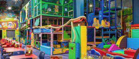 Un área de juegos infantiles con estructuras para escalar, toboganes y mesas con sillas.