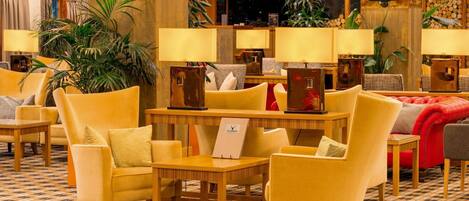 Eine Hotelhalle mit gelben Sesseln, Holztischen und einer Rezeption.