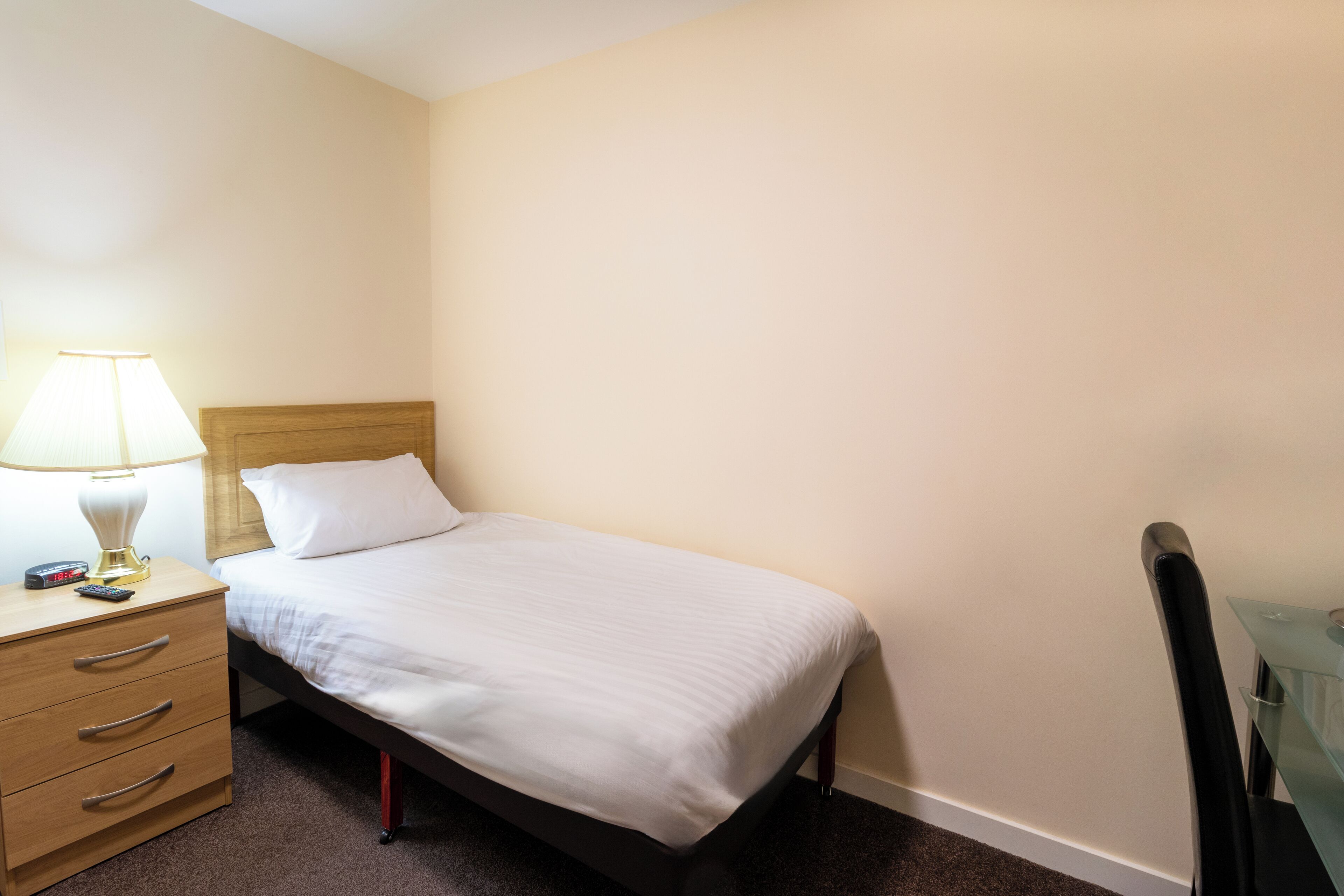 A single bed with a wooden headboard, a bedside table with a lamp, and a chair.