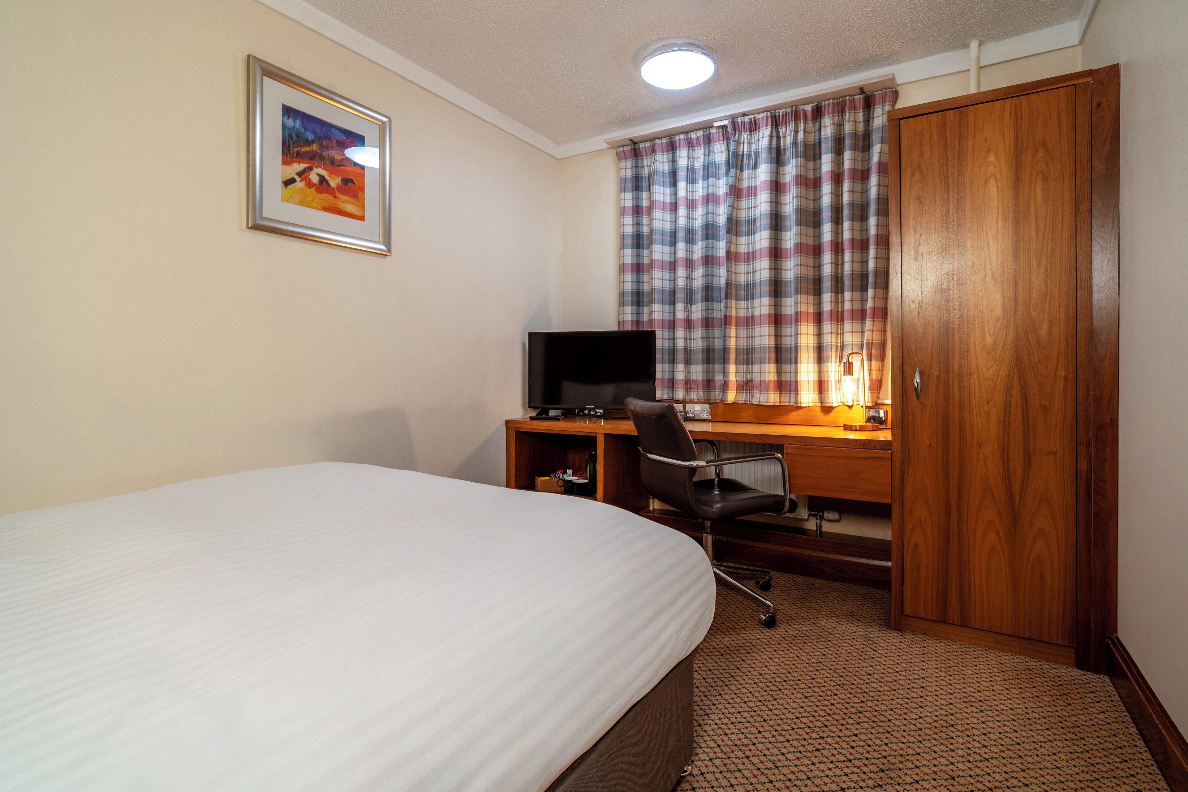 Een hotelkamer met een bed, een bureau met een computer, een stoel en een kledingkast.