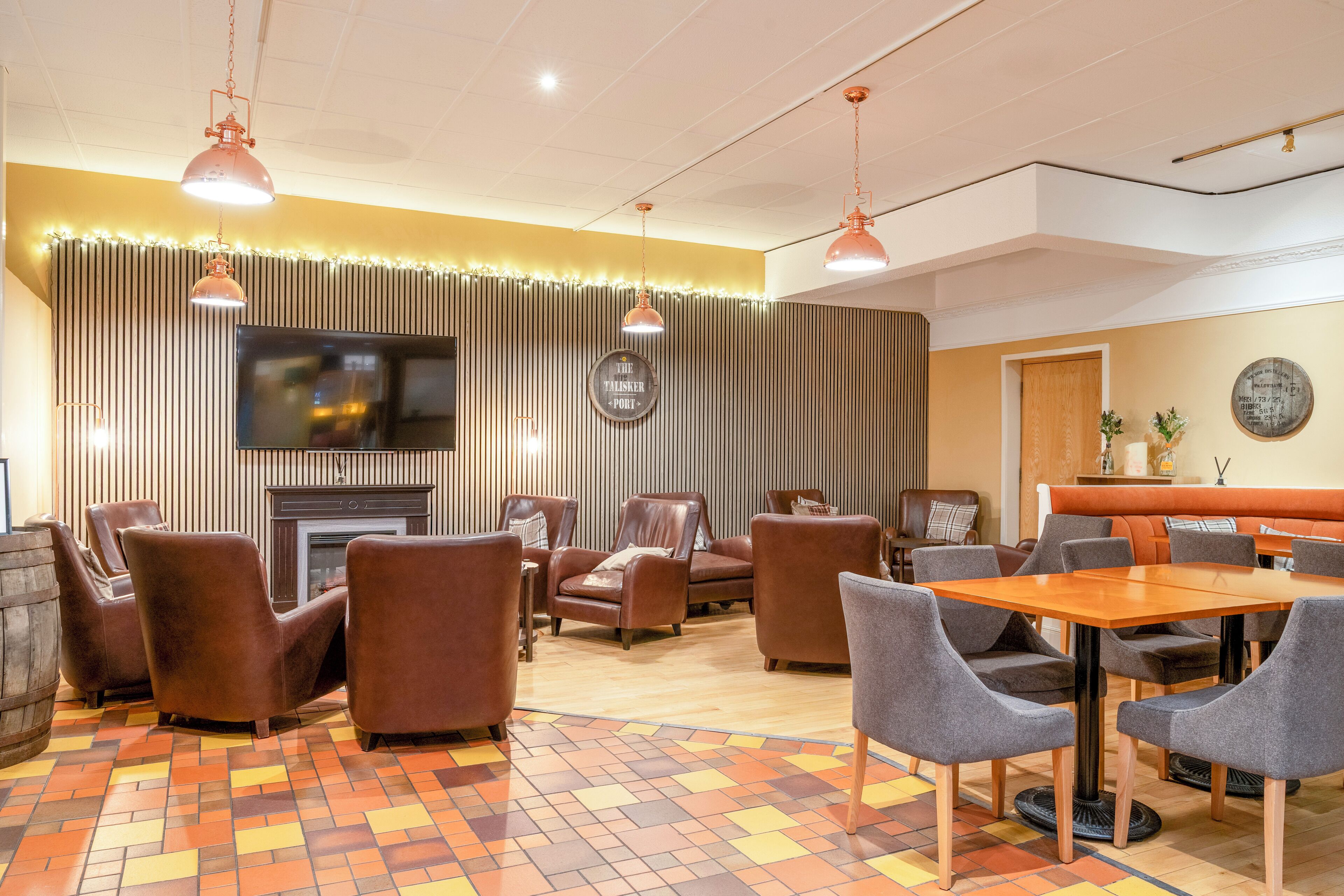 A hotel lobby with leather armchairs, a wooden table, and a television mounted on the wall.