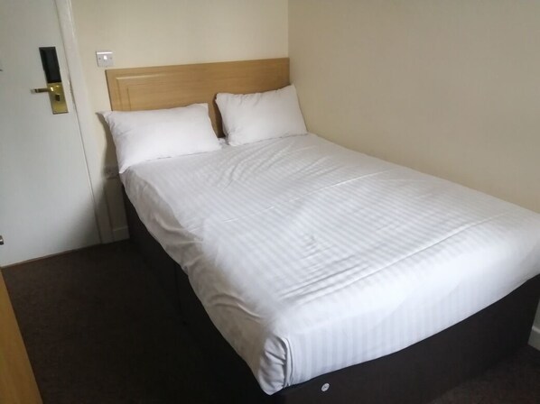 A single bed with a wooden headboard, white bedding, and a plain wall.
