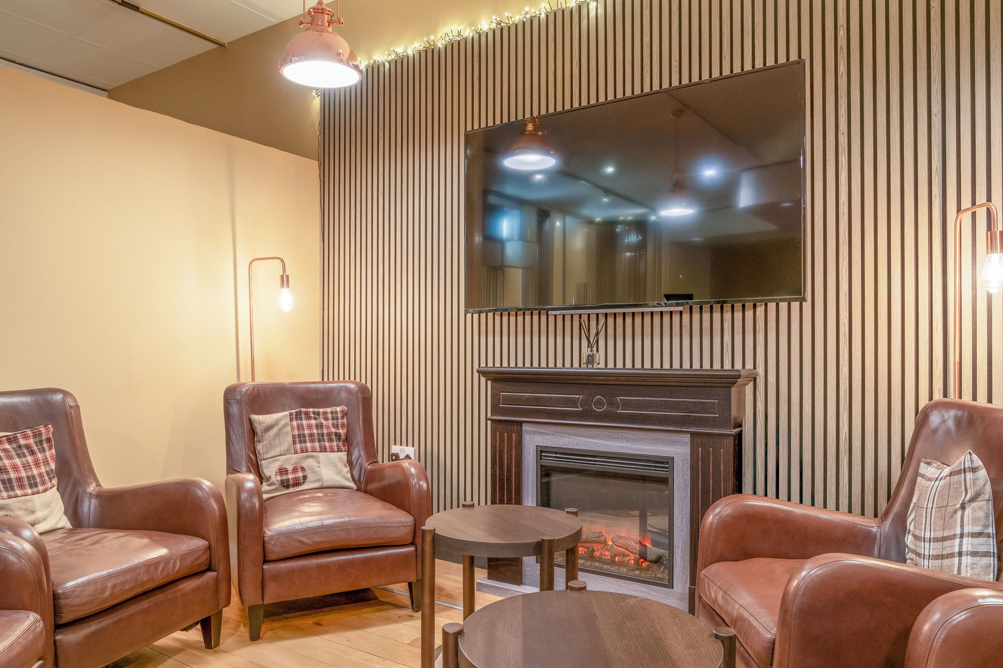 Una sala de estar acogedora con sillones de cuero, una chimenea y un televisor de pantalla plana montado en una pared de madera.