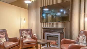 A cozy living room with leather armchairs, a fireplace, and a flat-screen TV mounted on a wooden wall.