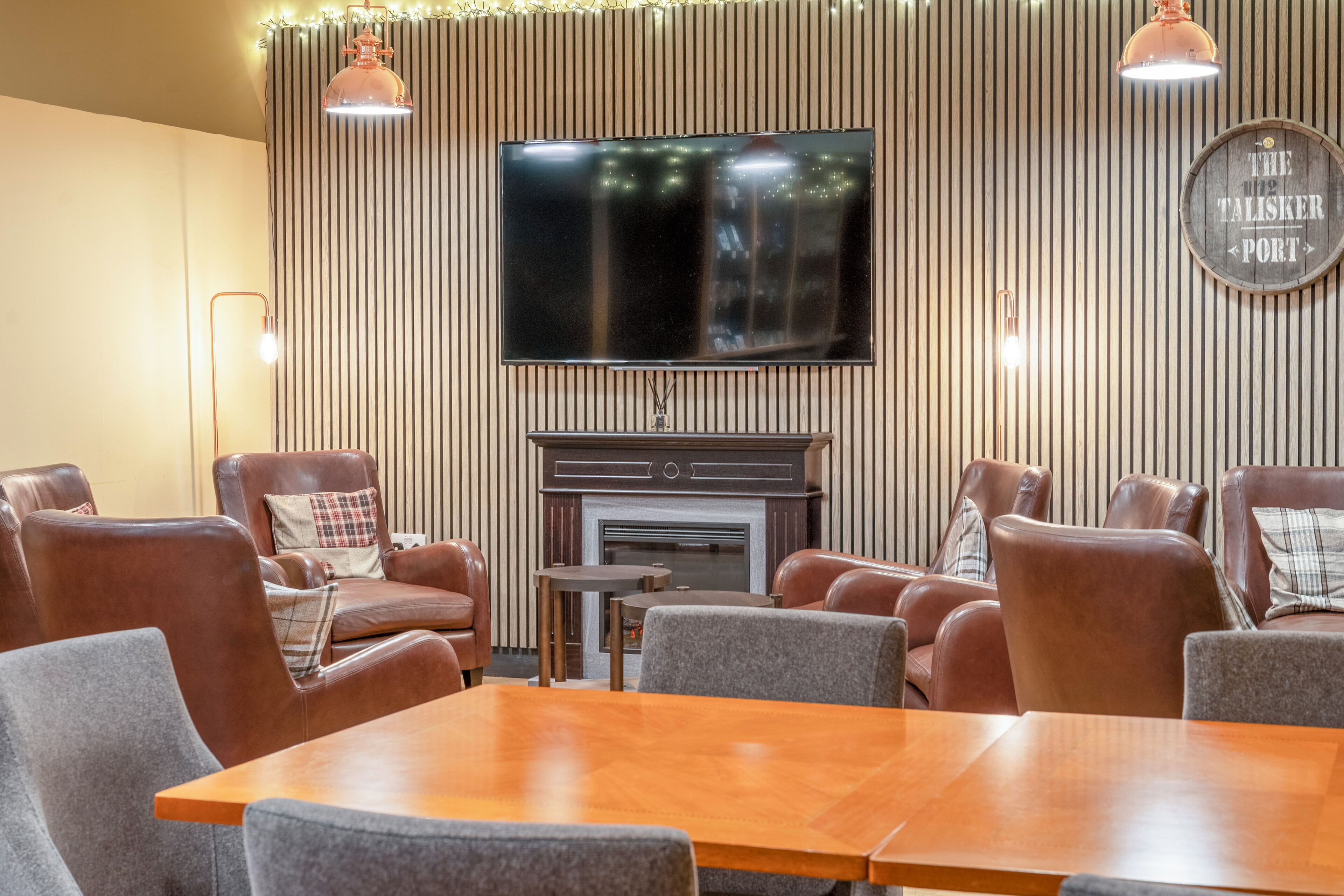 A modern living room with leather sofas, a wooden coffee table, a flat-screen TV mounted on a striped wall, and a fireplace.