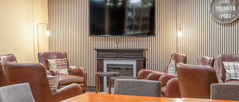 A modern living room with leather sofas, a wooden coffee table, a flat-screen TV mounted on a striped wall, and a fireplace.