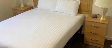 A neatly made bed with white linens, two bedside tables with lamps, and a wooden headboard.