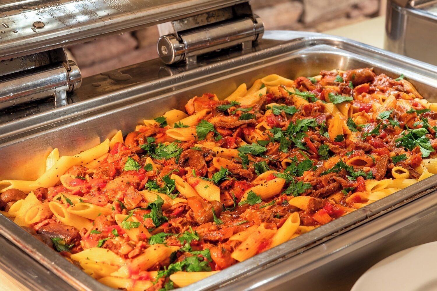 Un buffet con piatti di pasta, tra cui penne al ragù, guarnite con prezzemolo.