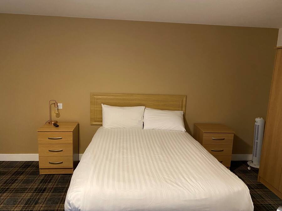 Una habitación de hotel con una cama grande, dos mesitas de noche, una lámpara y un calentador.