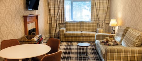 A cozy living room with a plaid sofa, a small round table, and a television mounted on the wall.