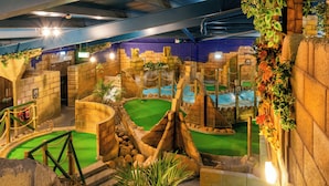 An indoor play area with artificial rock formations, green turf, and climbing structures.