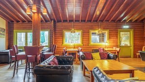A log cabin interior with wooden beams, leather furniture, and a dining area.
