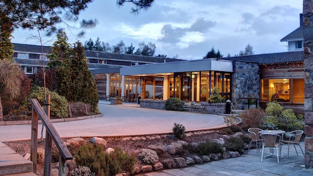 A modern building with a glass facade, stone exterior, and outdoor seating area.